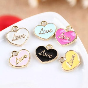 May include: Six heart-shaped charms with gold-coloured metal frames and different coloured enamel finishes. Each charm features the word "Love" written in a cursive script. The charms are white, light blue, pink, black, yellow, and pink.
