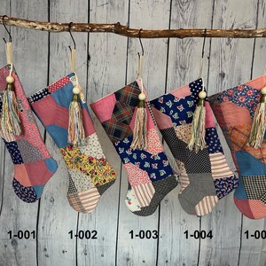 May include: Five patchwork Christmas stockings with pink, blue, and white fabric. Each stocking has a wooden bead and a tassel. The stockings are labeled 1-001 through 1-005.
