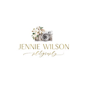 Op de afbeelding: Een aquarel-illustratie van een vintage camera met een bloemstuk van witte bloemen en bruine bladeren. De tekst "Jennie Wilson photography" is in gouden schrift onder de camera geschreven.