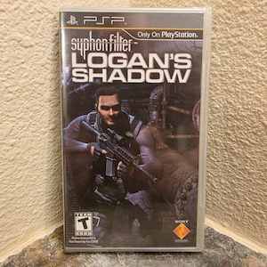 Peut inclure: Un boîtier de jeu PlayStation Portable scellé pour Syphon Filter: Logan's Shadow. La jaquette présente un personnage tactique sombre tenant un fusil dans un décor industriel. Le texte inclut le titre du jeu, le logo PSP et la classification ESRB Teen.