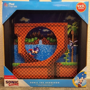 May include: A Pixel Frames Sonic the Hedgehog shadow box art measuring 9x9 inches. The black-framed display features a multi-layered 3D scene of Sonic running through a checkered loop, with a waterfall, palm tree, and enemy character in the background.