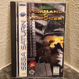 May include: A Sega Saturn video game case for Command & Conquer by Westwood Studios. The cover features a black and white graphic of a soldier in goggles with an orange explosion, a red starburst label stating 2 CDs of World Domination, and an ESRB Teen rating.