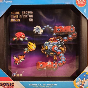 May include: A 9x9 inch Sonic the Hedgehog shadow box art featuring a pixelated battle scene with Knuckles, Tails, and Super Sonic fighting Dr. Eggman in his machine. The display includes game stats like score, time, and rings in the top left corner.