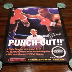 Könnte beinhalten: Ein rechteckiges Poster für das Videospiel Mike Tyson's Punch-Out!! für das Nintendo Entertainment System. Es zeigt eine Boxkampfszene mit Mike Tyson in roten Handschuhen, einen Schiedsrichter und den Spieltitel in großer weißer Schrift.