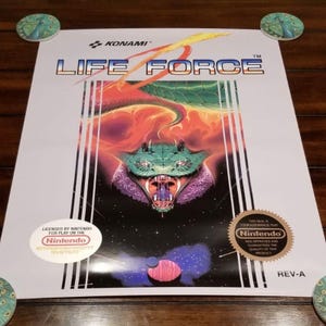 May include: A rectangular Life Force video game box cover featuring the Konami logo, a central green serpent head with an open mouth, orange and red flames, and a dark space background. It includes the Nintendo seal and licensing text.