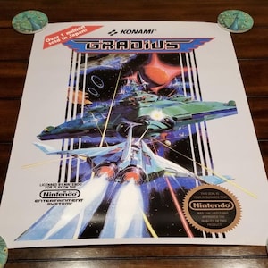 Könnte beinhalten: Ein Gradius Videospiel-Poster mit einer Weltraumschlacht, einem Raumschiff, das Laser abfeuert, dem Konami-Logo, dem Text Over 1 million sold in Japan, dem Nintendo Entertainment System-Logo und dem offiziellen Nintendo-Qualitätssiegel.