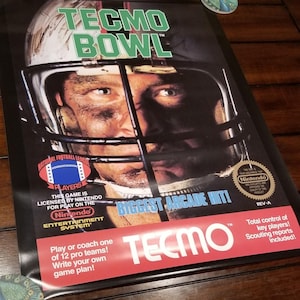 以下が含まれることがあります： Tecmo Bowlの長方形のビデオゲームボックスカバー。フェイスマスク付きヘルメットを被ったフットボール選手が描かれている。テキストにはTecmo Bowl、Biggest Arcade Hitとあり、任天堂とNFLのロゴが含まれている。