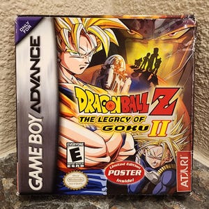 May include: A Game Boy Advance video game box for Dragon Ball Z: The Legacy of Goku II. The cover features Goku and Trunks with yellow hair, the Dragon Ball Z logo, an ESRB E rating, an Atari logo, and a red sticker stating Limited Edition Poster Inside.
