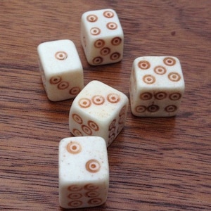 May include: Five white dice with brown circles on each face. The dice are on a wooden surface.