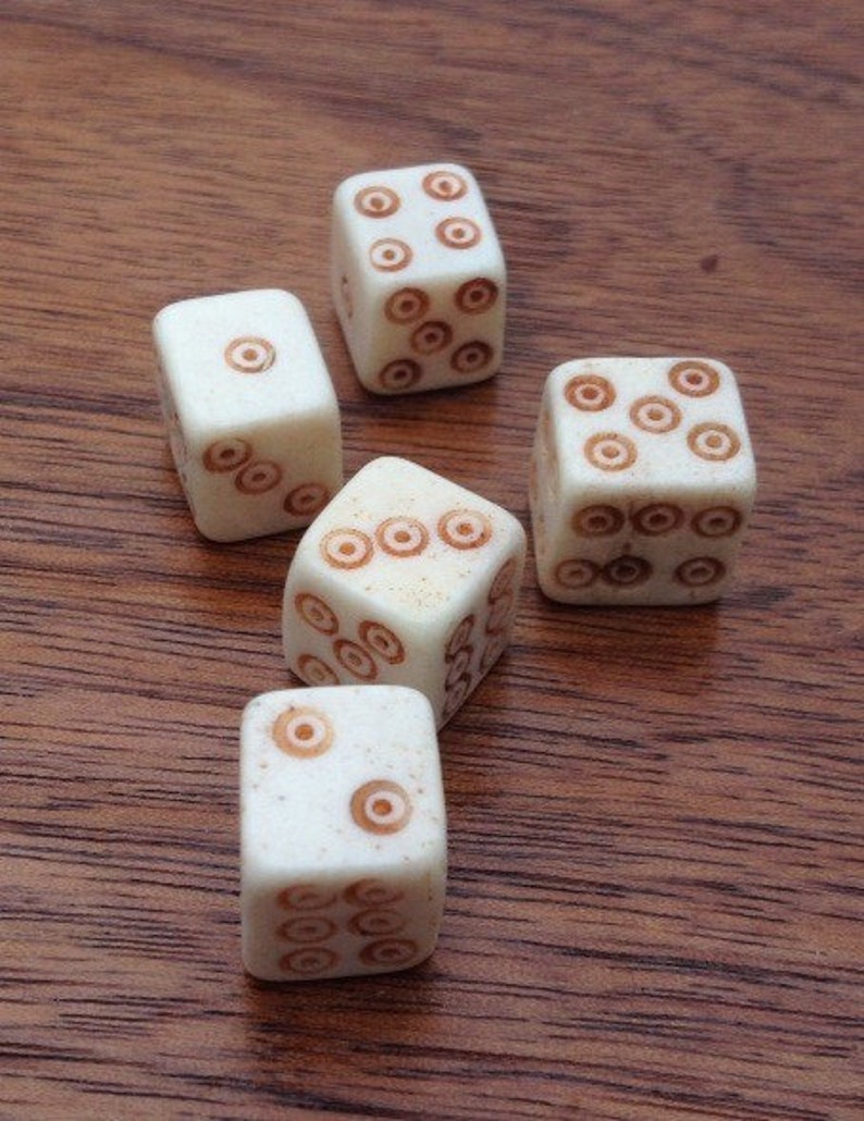 May include: Five white dice with brown circles on each face. The dice are on a wooden surface.
