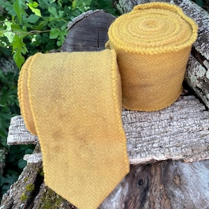 May include: A roll of yellow wool fabric with a herringbone pattern. The fabric is rolled up and tied with a ribbon. The fabric is on a wooden surface.