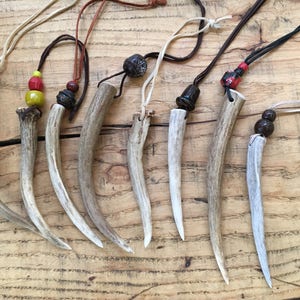 Puede incluir: Ocho colgantes de asta de ciervo con cuentas y cordones de varios colores. Las astas son todas blancas y tienen un acabado natural y pulido. Los cordones son de cuero y gamuza.