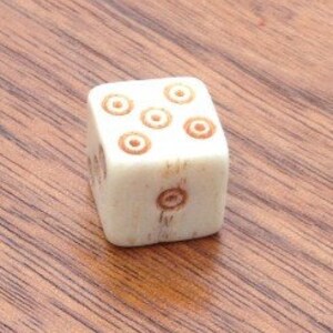 May include: A white wooden dice with brown circles on each side. The dice has a total of six circles.