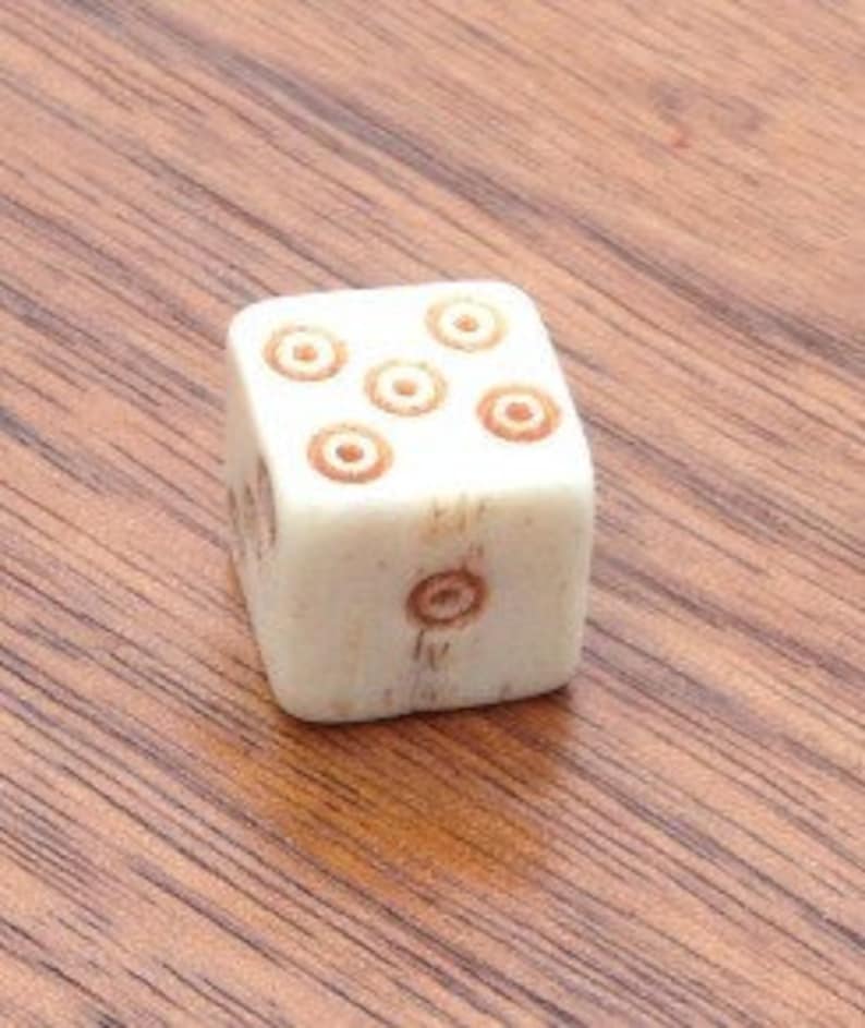 May include: A white wooden dice with brown circles on each side. The dice has a total of six circles.