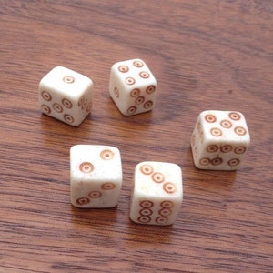 May include: Five white dice with brown circles on each face. The dice are arranged in a semi-circle on a wooden surface.