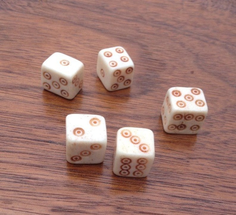 May include: Five white dice with brown circles on each face. The dice are arranged in a semi-circle on a wooden surface.