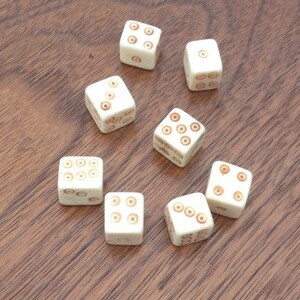 May include: Eight white dice with brown dots on each side. The dice are arranged in a semi-circle on a wooden surface.