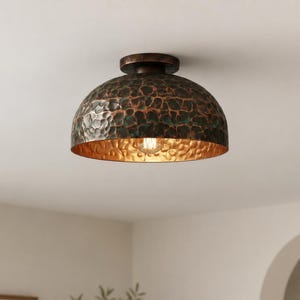 May include: A semi-flush mount ceiling light fixture featuring a dome-shaped shade with a hammered metal texture. The exterior has a dark, oxidized copper finish with green patina accents, while the interior has a warm, reflective gold tone.