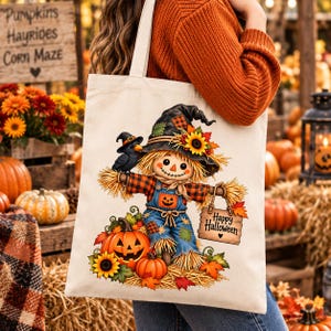 Puede incluir: Un bolso de tela color crema con un gráfico colorido de un espantapájaros con sombrero, camisa de cuadros, peto azul con un parche de calabaza y detalles de paja. Un cuervo negro se posa sobre su hombro y sostiene un cartel que dice Happy Halloween.