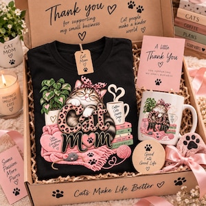 Puede incluir: Una camiseta negra con el gráfico de un gato con diadema y gafas de estampado de leopardo rosa, descansando sobre libros y una manta rosa. El diseño incluye el texto Cat Mom, una taza de café, una planta y un ratón en una caja de regalo.