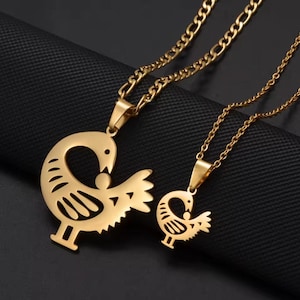 Könnte beinhalten: Zwei goldfarbene Halsketten mit vogelformigen Anhängern. Die Anhänger haben ein ausgeschnittenes Design eines Vogels, der nach links blickt, mit einem kleinen Kreis in der Mitte. Die Halsketten befinden sich auf einem schwarzen Hintergrund.