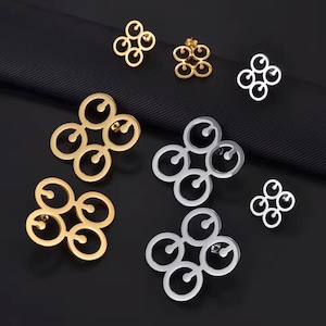May include: A collection of stud earrings featuring a four-circle clover-like design. The set includes gold-toned and silver-toned metal pieces in varying sizes, each with a post back closure and a circular cutout pattern within each ring segment.