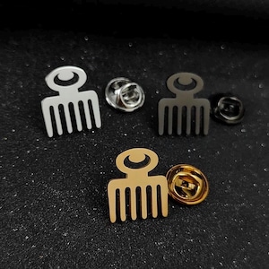 Könnte beinhalten: Drei Metall-Anstecknadeln in Form von Haarkämmen mit kreisförmigem Oberteil. Das Set enthält eine silberfarbene, eine schwarze und eine goldfarbene Nadel, jeweils mit passendem Metall-Schmetterlingsverschluss zur sicheren Befestigung am Stoff.