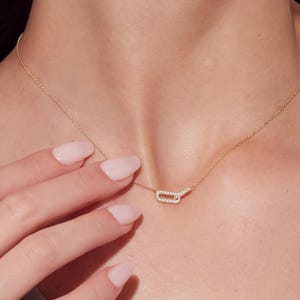 May include: A gold chain necklace featuring a small, rectangular pendant link encrusted with tiny, clear, sparkling stones. The pendant is connected to a delicate gold chain that rests against the skin, creating a refined and simple jewelry piece.