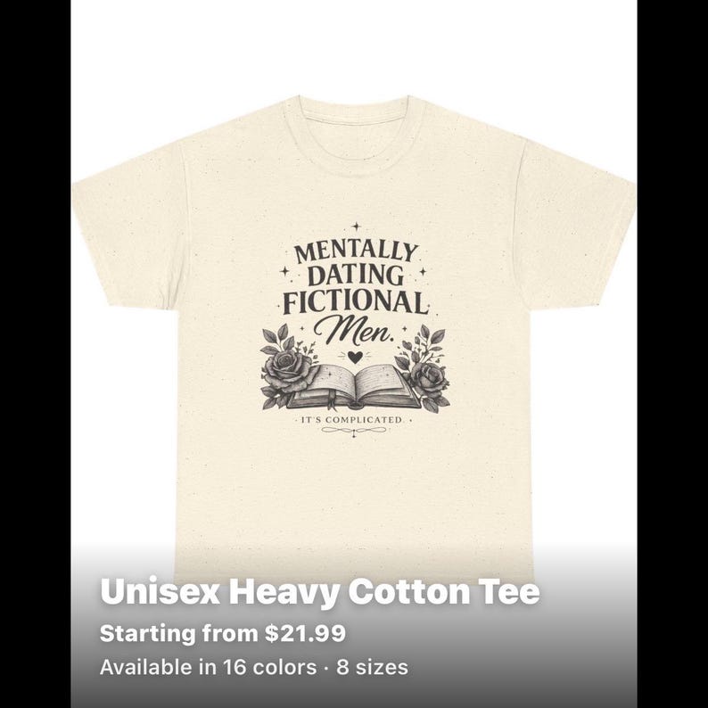 May include: A cream-coloured short-sleeve t-shirt with a speckled texture. The front features a black graphic of an open book flanked by roses, with the text "MENTALLY DATING FICTIONAL Men." and "IT'S COMPLICATED." printed in a decorative font.