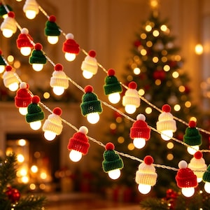 May include: A string of LED fairy lights featuring miniature knitted beanies in red, green, and white. Each beanie is topped with a small pom-pom and covers a glowing light bulb. The festive decorative strand is arranged in multiple loops.