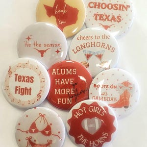 May include: A collection of nine round pinback buttons featuring various designs in shades of orange, red, and white. The buttons display text including 'Texas Fight', 'ALUMS HAVE MORE FUN', 'CHOOSIN TEXAS', 'tis the season', and 'HOT GIRLS THE HORNS'.