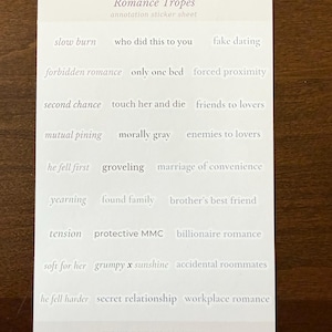 Op de afbeelding: Een rechthoekig wit stickervel met de titel Romance Tropes annotation sticker sheet. Het bevat rijen met individuele tekststickers, waaronder slow burn, fake dating, forbidden romance, only one bed, forced proximity, second chance, touch her and die, friends to lovers, mutual pining, morally gray, enemies to lovers, he fell first, groveling, marriage of convenience, yearning, found family, brother's best friend, tension, protective MMC, billionaire romance, soft for her, grumpy x sunshine, accidental roommates, he fell harder, secret relationship, workplace romance en The Midnight Escapes Studio.