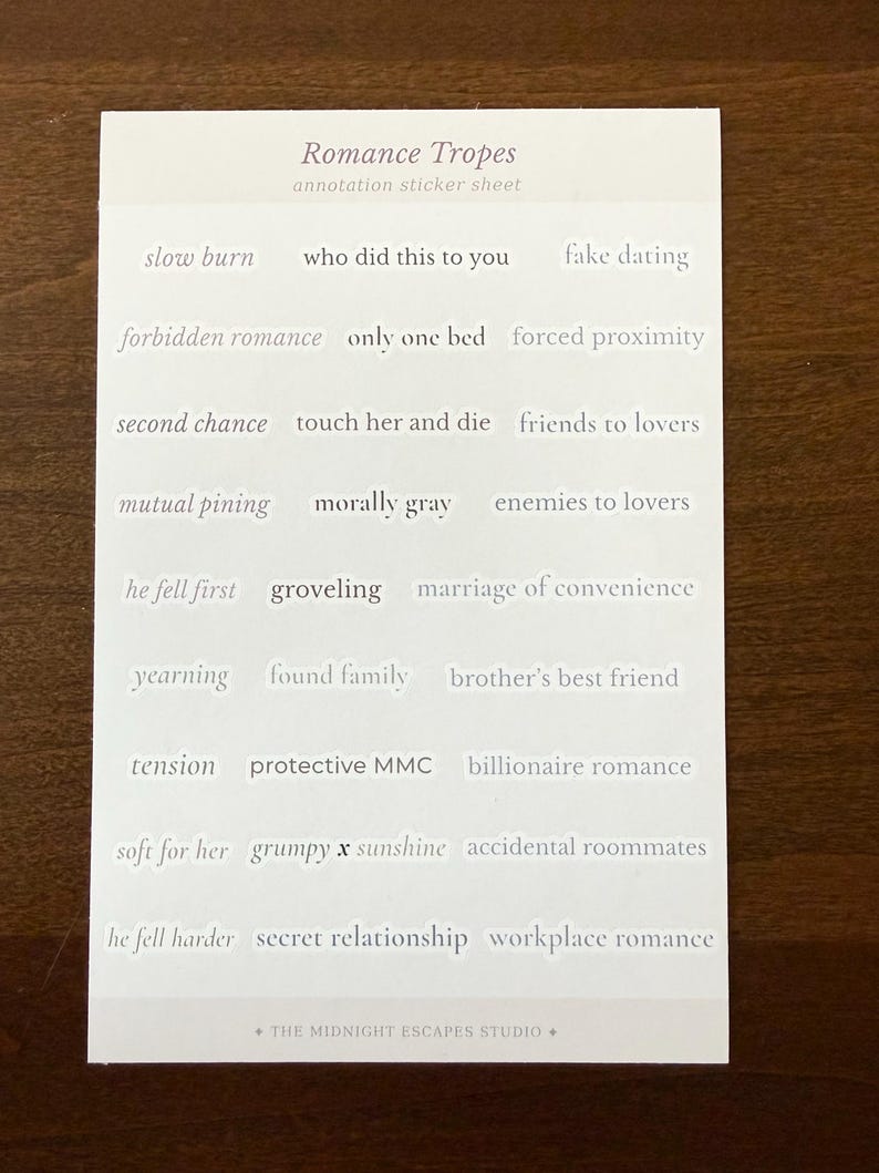 Op de afbeelding: Een rechthoekig wit stickervel met de titel Romance Tropes annotation sticker sheet. Het bevat rijen met individuele tekststickers, waaronder slow burn, fake dating, forbidden romance, only one bed, forced proximity, second chance, touch her and die, friends to lovers, mutual pining, morally gray, enemies to lovers, he fell first, groveling, marriage of convenience, yearning, found family, brother's best friend, tension, protective MMC, billionaire romance, soft for her, grumpy x sunshine, accidental roommates, he fell harder, secret relationship, workplace romance en The Midnight Escapes Studio.