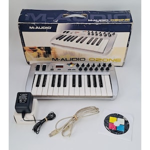 May include: M-Audio Ozone USB audio and MIDI mobile workstation keyboard with 25 keys, control knobs, sliders, and a digital display. Includes a black AC power adapter, a USB cable, a software disc, and the original branded cardboard box.