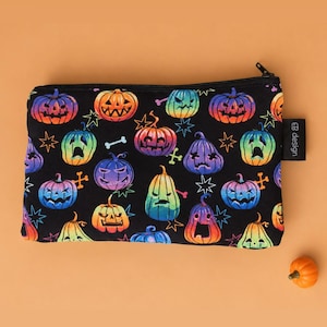 May include: A rectangular black zipped pouch featuring a repeating pattern of colourful gradient pumpkins in shades of orange, yellow, green, blue, and purple, accented with small stars and bones. A small black tag with the text "CB design" is attached.