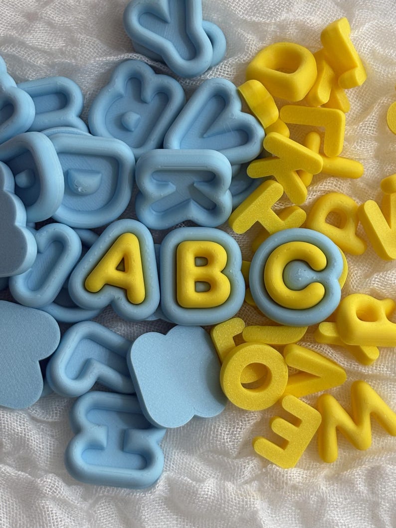 May include: A collection of small, three-dimensional alphabet letters in light blue and bright yellow. The letters are scattered, with the letters A, B, and C prominently displayed in the center, featuring yellow characters set against light blue frames.