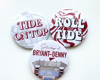 May include: Three circular pin-back buttons. One features a silver disco ball pattern with the red text TIDE ON TOP. Another has a red and white swirl design with the text ROLL TIDE. The third shows a stadium illustration with the text Saturdays at BRYANT-DENNY.