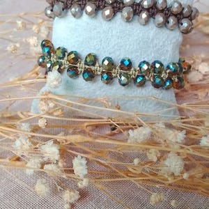 Peut inclure: Deux bracelets de perles composés de perles à facettes aux tons métalliques tissées sur un cordon. Le bracelet supérieur présente des perles marron clair sur un cordon marron foncé, tandis que celui du bas a des perles irisées sur un cordon beige.