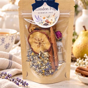 May include: A kraft paper pouch labeled London Fog Simmer Pot containing dried pear slices, cinnamon sticks, a dried rosebud, loose lavender, and chamomile flowers, with a small clear vial of liquid attached to the front.