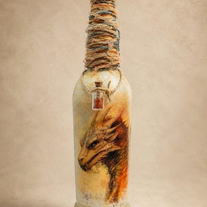 May include: A decorative glass bottle featuring a detailed illustration of a golden dragon on the front. The neck is wrapped in textured orange and blue fibers, topped with a circular cap, and adorned with a small glass vial containing red stones.
