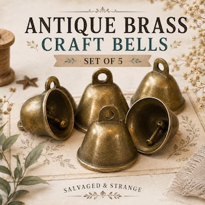 May include: A set of five antique brass craft bells with a weathered finish. Each bell features a rounded dome shape, a top loop for hanging, and an internal clapper. The text "ANTIQUE BRASS CRAFT BELLS SET OF 5" and "SALVAGED & STRANGE" is visible.