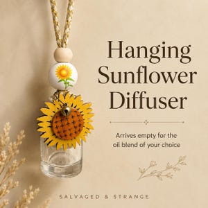 May include: A hanging sunflower diffuser with a clear glass bottle, a wooden bead painted with a sunflower, and a yellow wooden sunflower charm featuring a small metal bell. The text reads Hanging Sunflower Diffuser, Arrives empty for the oil blend of your choice, and SALVAGED & STRANGE.