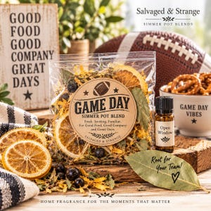 May include: A clear plastic pouch containing a Game Day simmer pot blend of dried orange slices, bay leaves, and dark berries. The label features a football graphic and text. Beside it sits a small amber glass bottle labeled Open Window.