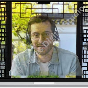 May include: A laptop screen showing a person wearing glasses and headphones, framed by a decorative window with a geometric design. The background features greenery and a building.