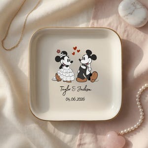 May include: A square cream-colored ceramic trinket dish with a gold-toned rim. The center features a graphic of two cartoon mice in wedding attire, three red hearts, and the printed text Taylor & Jackson followed by the date 04.06.2026.