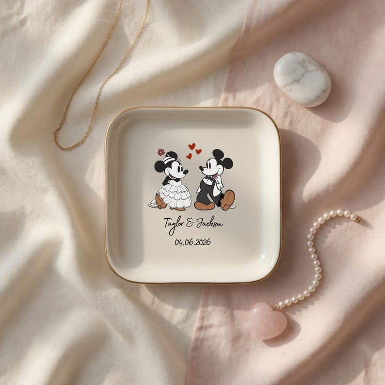 May include: A square cream-colored ceramic trinket dish with a gold-toned rim. The center features a graphic of two cartoon mice in wedding attire, three red hearts, and the printed text Taylor & Jackson followed by the date 04.06.2026.