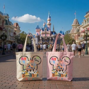 Pu&ograve; includere: Due borse tote, una color crema e una rosa chiaro, ciascuna con la grafica di un castello all'interno di una silhouette delle orecchie di Topolino, con il testo "Disney Trip" e "2026" sotto e un nome scritto in corsivo in alto.