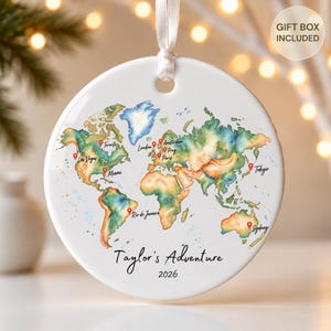 May include: A round white ceramic ornament featuring a watercolor world map with red location pins marking cities including Toronto, Las Vegas, Miami, London, Amsterdam, Prague, Paris, Rio de Janeiro, Tokyo, and Sydney. Text reads Taylor's Adventure 2026.