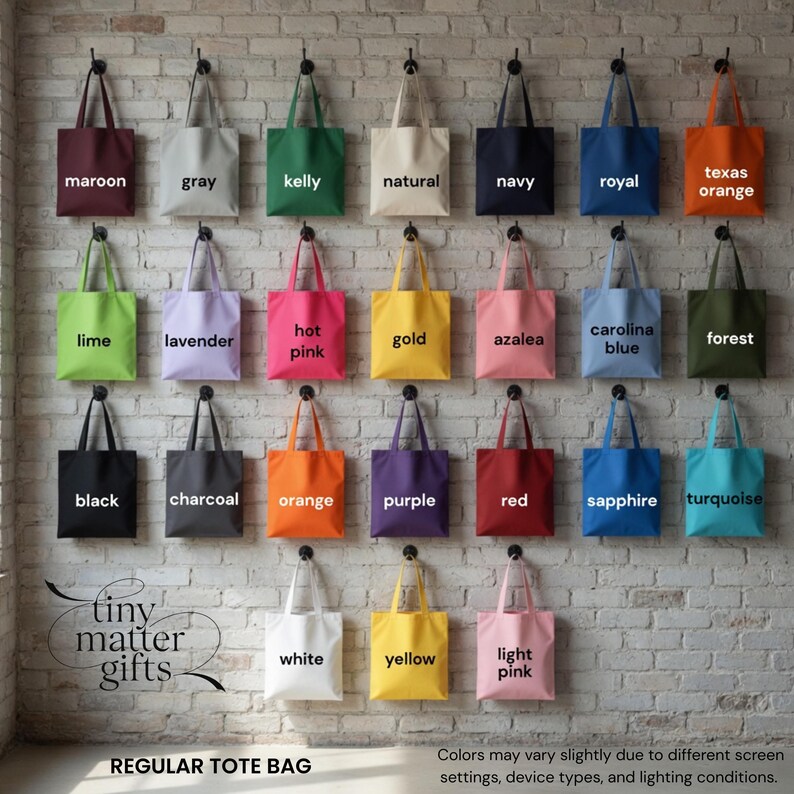 Pu&ograve; includere: Una collezione di venticinque borse tote in tela a tinta unita appese a una parete di mattoni. Ogni borsa presenta un'etichetta stampata che ne identifica il colore, tra cui marrone, grigio, kelly, naturale, blu navy, blu reale, arancione texas, lime, lavanda, rosa acceso, oro, azalea, blu carolina, foresta, nero, antracite, arancione, viola, rosso, zaffiro, turchese, bianco, giallo e rosa chiaro.