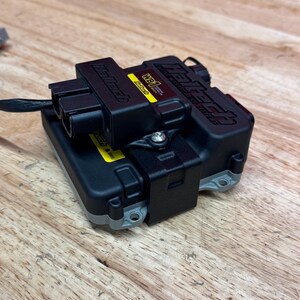 May include: A black Haltech WB1 wideband controller with a yellow sticker and the Haltech logo. The controller is on a wooden surface.